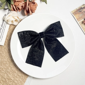 Detail of a large black sequined bow hair clip with shimmering texture on a decorative plate