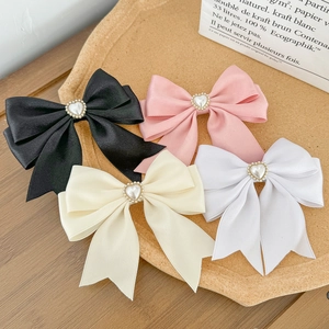 Detailed close-up of bow hair clips with heart pearls in black, pink, beige, and white