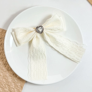 Close-up of cream lace bow hair clip featuring a sparkling heart crystal in the center