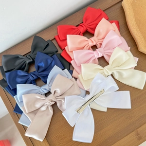 Elegant satin bow hair clip set in multiple colors like red, pink and cream on wood base