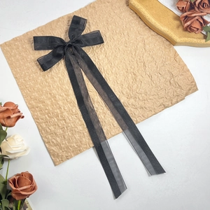 Detail einer eleganten schwarzen Haarklammer aus Organza mit langen Bändern auf Papier