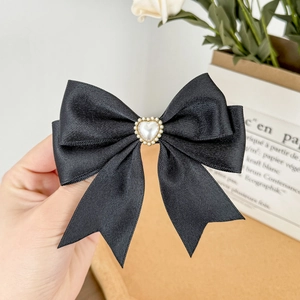 Close-up of a layered black satin bow hair clip with a pearl heart-shaped centerpiece