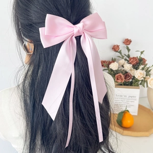 Detail of pink satin ribbon bow hair clip worn in a stylish half-up hairstyle