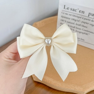 Detail of cream satin bow hair clip with heart-shaped pearl and gold scalloped trim