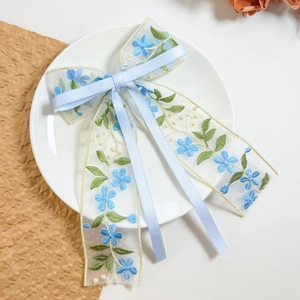 Detail of light blue organza bow hair clip with floral embroidery and long ribbons