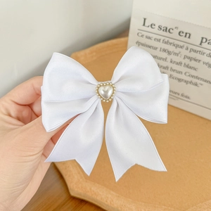 Detailed close-up of white satin bow hair clip with heart-shaped faux pearl embellishment