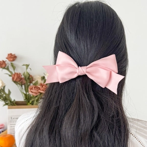 Rear view of a model wearing the pink double-layer satin bow hair clip on dark curly hair