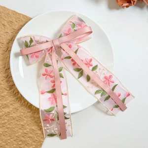 Detail of pink organza hair clip with floral embroidery and elegant bow ribbons
