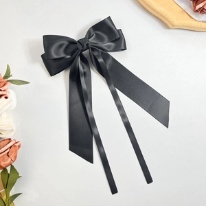 Detail view of smooth black satin bow hair clip with long flowing ribbons on white background