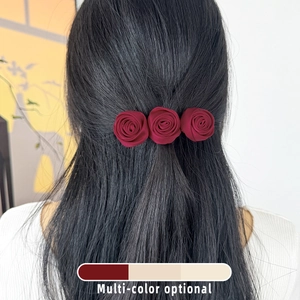 Detail of three wine red satin handmade roses on hair clip worn on black hair