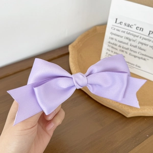 Detail of a purple satin double-layered bow hair clip with elegant glossy texture