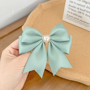 Detail showing mint green satin bow hair clip with heart pearl decoration