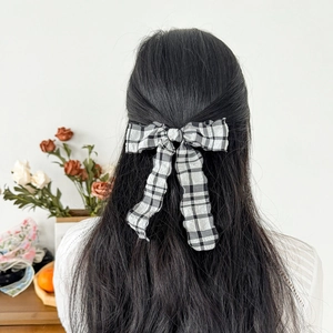 Elegant black and white checkered bow hair clip with long ribbons worn by a model