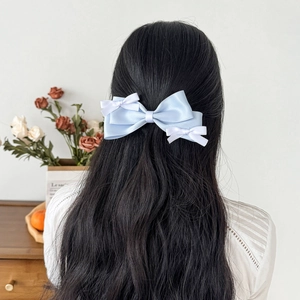 Light blue satin bow hair clip with small white accents worn on a woman's dark hair