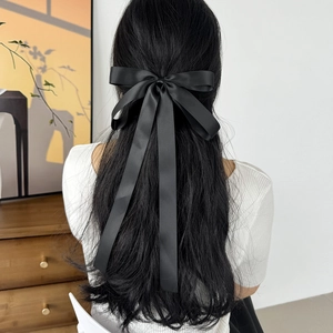 Elegant black satin bow hair clip with long ribbons worn by a model in a minimal room