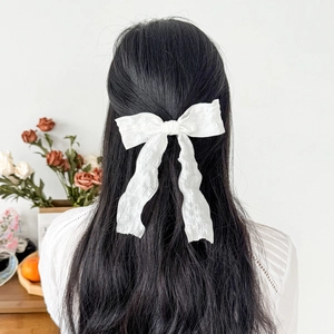 Large white bow hair clip with elegant streamers shown on back of model's head