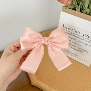 Detailed view of a soft pink satin bow hair clip held in hand with a silk texture