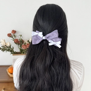 Detail of a large purple satin bow hair clip with small white bows on black wavy hair