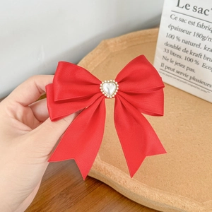 Detailed close-up of a red satin bow hair clip with a centered heart pearl in hand