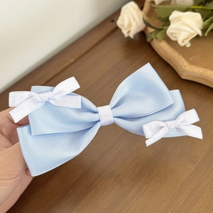 Detailed close-up of light blue silk bow hair clip with small white decorative accents