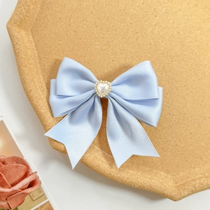 Detail of light blue satin bow hair clip with a central pearl heart on a tray