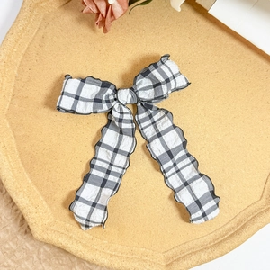 Detailed view of a sweet checkered bow hairclip with elegant black wavy edges on a tray
