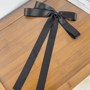 Detailed shot of a black satin ribbon bow hair clip with long tails on a wooden tray