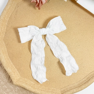 Detail of white textured fabric bow hair clip with long ribbons on a wooden tray