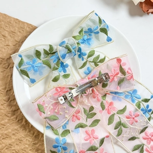 Dettagli ricamati su fermagli per capelli in organza con motivi floreali e clip metalliche