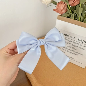 Detail view of light blue satin bow hair clip held against a French vintage background