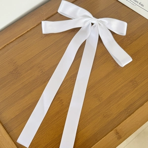 Detailed view of the white satin long ribbon bow hair clip on a wooden tray background