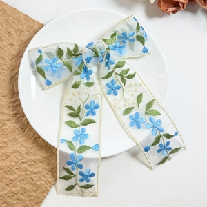 Dettaglio del fiocco in organza bianca con ricamo di fiori blu su un piatto di ceramica