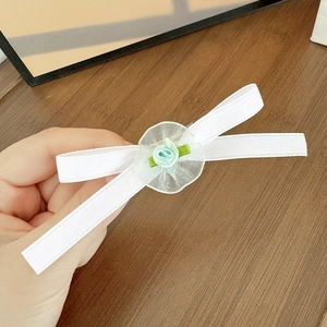 Dettaglio di un fermaglio per capelli con fiocco floreale in nastro bianco e fiore verde