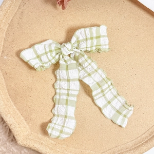 Detail of light green plaid bow hair clip with seersucker texture on a beige tray