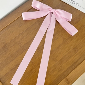 Detail of pink satin bow hair clip with long ribbons on a decorative wooden tray