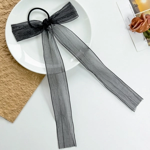 Detail shot of a black organza ribbon bow hair tie on a white plate with aesthetic decor