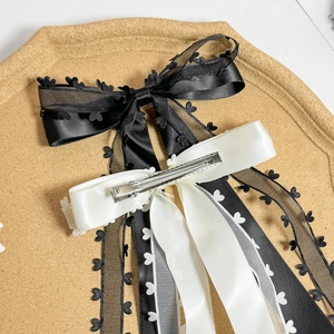 Elegant layered black and white bow hair clip with lace and satin on a cork tray