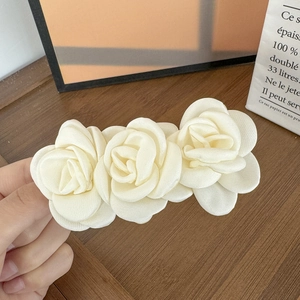 Détail de trois fleurs de camélia en satin crème sur une barrette à cheveux en tissu doux