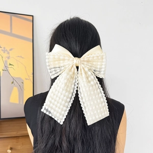 Detailed view of oversized beige lace bow hair clip on model's dark long straight hair