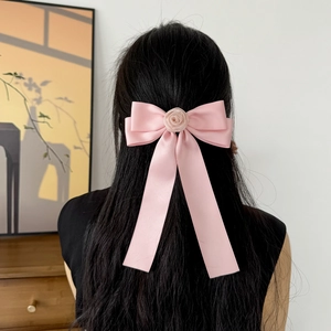 Barrette nœud en satin rose avec rose décorative portée sur de longs cheveux noirs