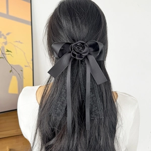 Detail view of black silk bow hair clip with rose accent and lace streamers on long hair