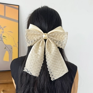 Detailed close-up of a large lace bow hair clip with floral embroidery on silk fabric