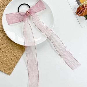 Detail of light pink mesh bow hair tie with long ribbons on a decorative white plate
