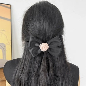 Dettaglio di un fiocco per capelli in raso nero con rosa rosa su capelli scuri vista retro
