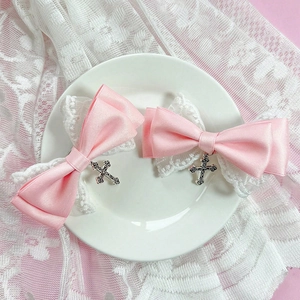 Detail einer rosa Satin-Spitzenschleife mit einem filigranen silbernen Kreuzanhänger