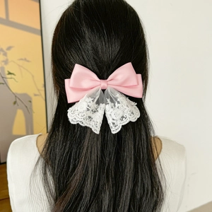 Detail of pink satin bow hair clip with intricate white lace trim on a woman's hair