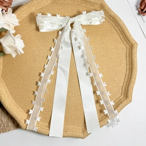 Detail of white satin and organza bow hair clip with hollow heart patterns on ribbon