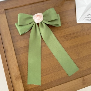 Détail d'un nœud en satin vert olive orné d'une petite rose en tissu rose au centre