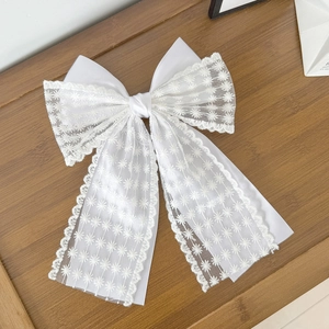 Elegant white lace bow hair clip with daisy embroidery and long tassels on wood
