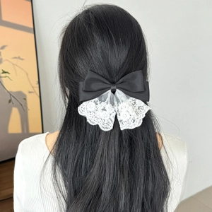 Detail of elegant black satin bow hair clip with white floral lace trim on dark hair